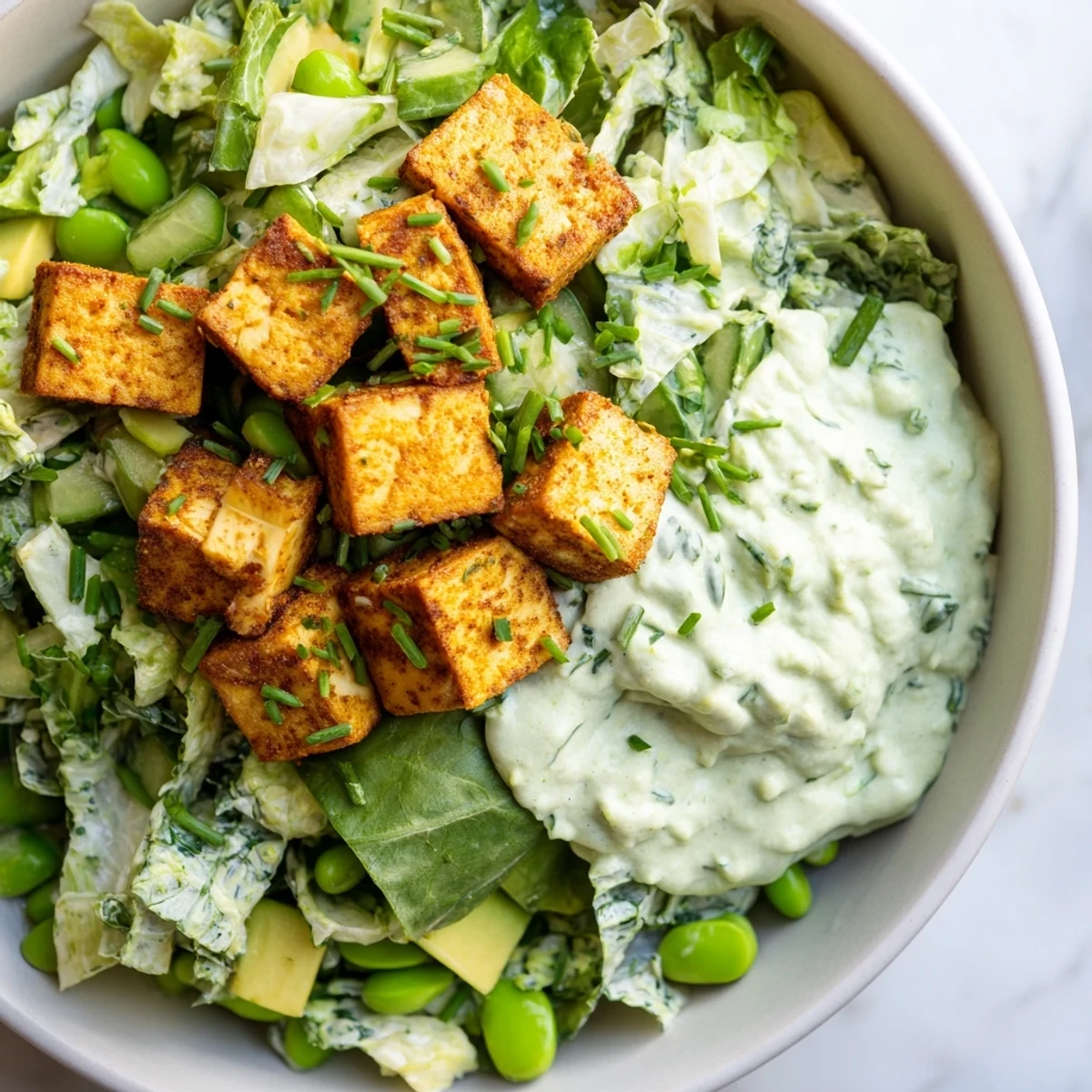 Golden, oven-baked tofu adds protein to this nutrient-packed Green Goddess Salad, garnished with fresh chives and a drizzle of zesty dressing.