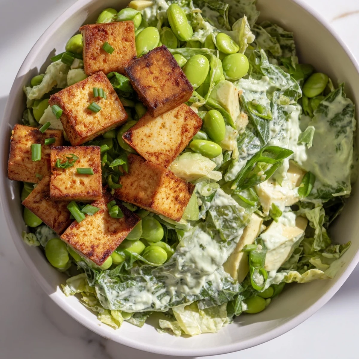 A hearty bowl of Green Goddess Salad with Baked Tofu, showcasing diced avocado, edamame, and crisp vegetables tossed in homemade dressing.