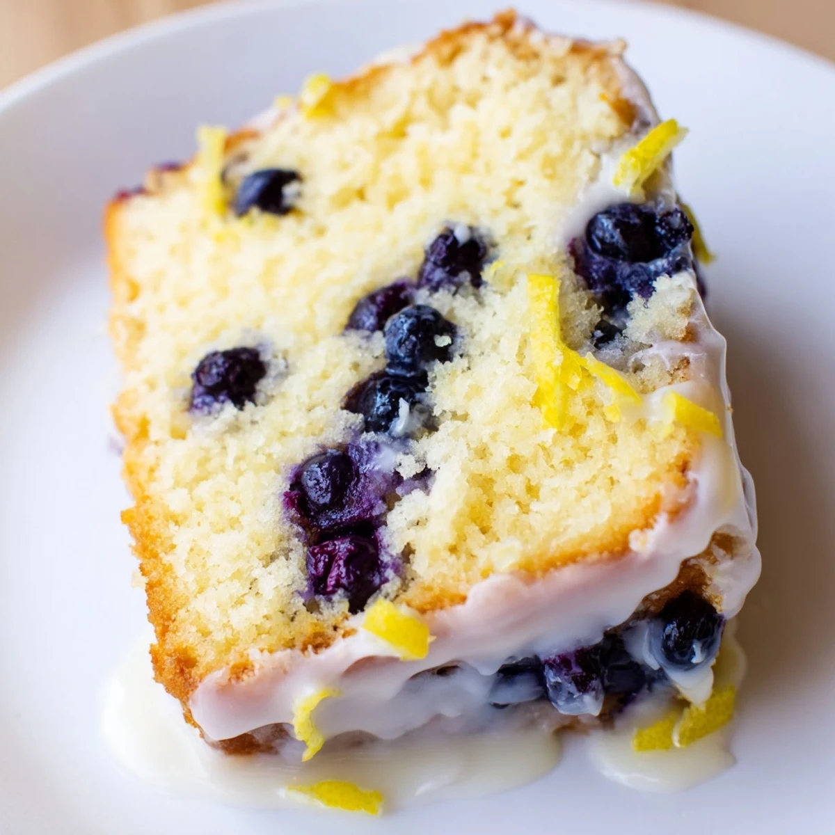 Warm Lemon Blueberry Coffee Cake slices drizzled with tangy glaze, garnished with lemon zest and fresh berries. 