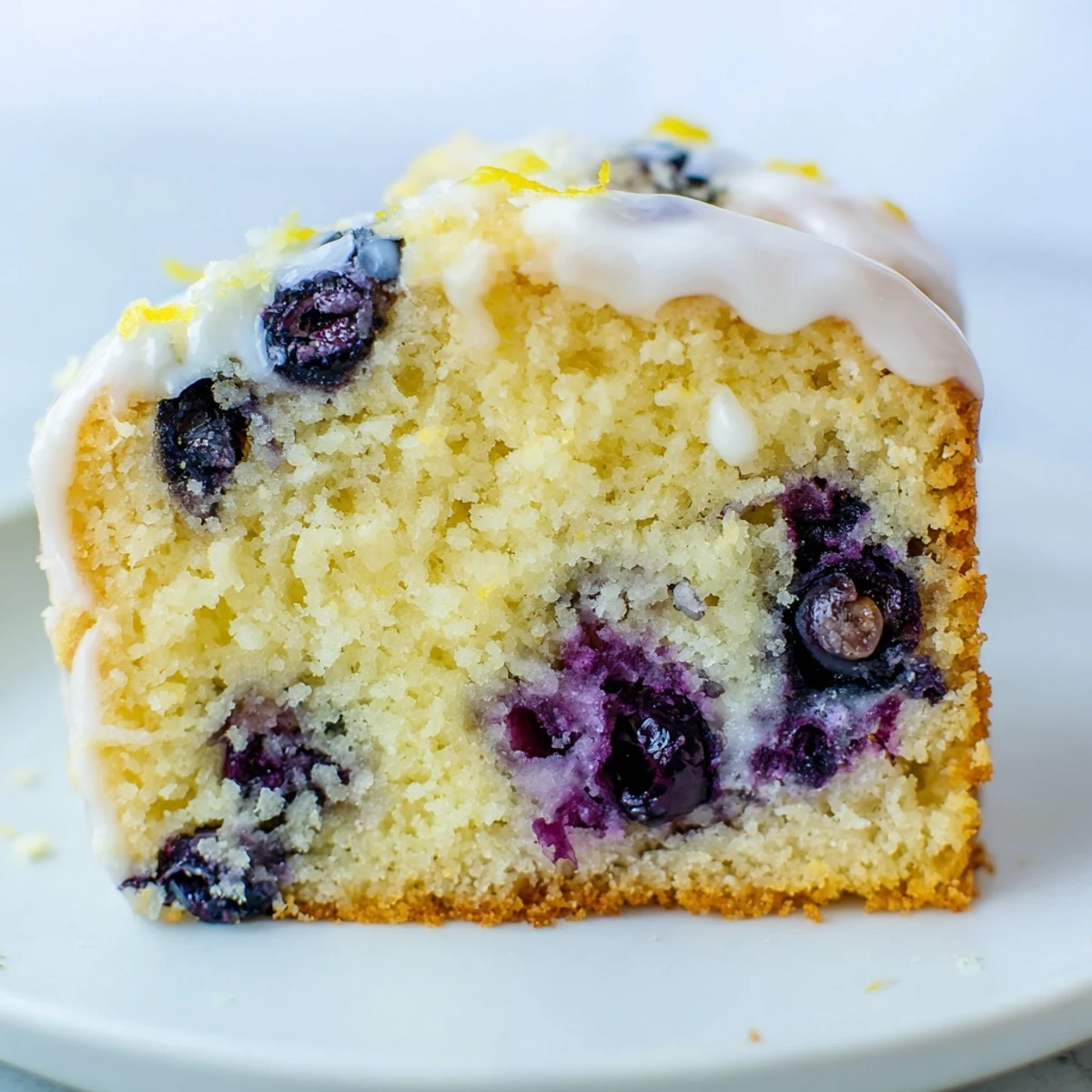 Freshly baked Lemon Blueberry Coffee Cake with glaze, topped with juicy blueberries and served on a white plate. 