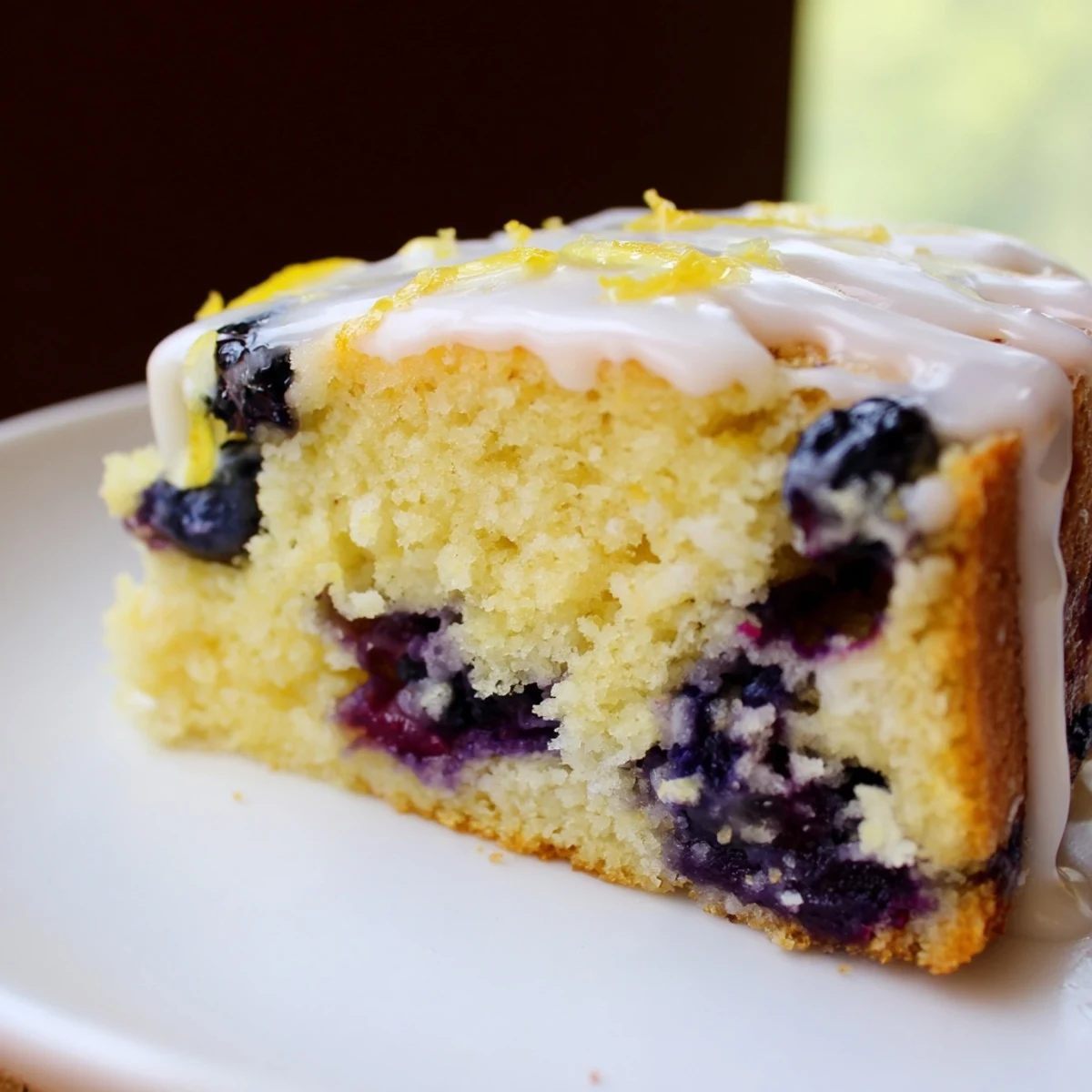 Moist Lemon Blueberry Coffee Cake with glaze on a rustic wooden board, fresh blueberries and lemon nearby.