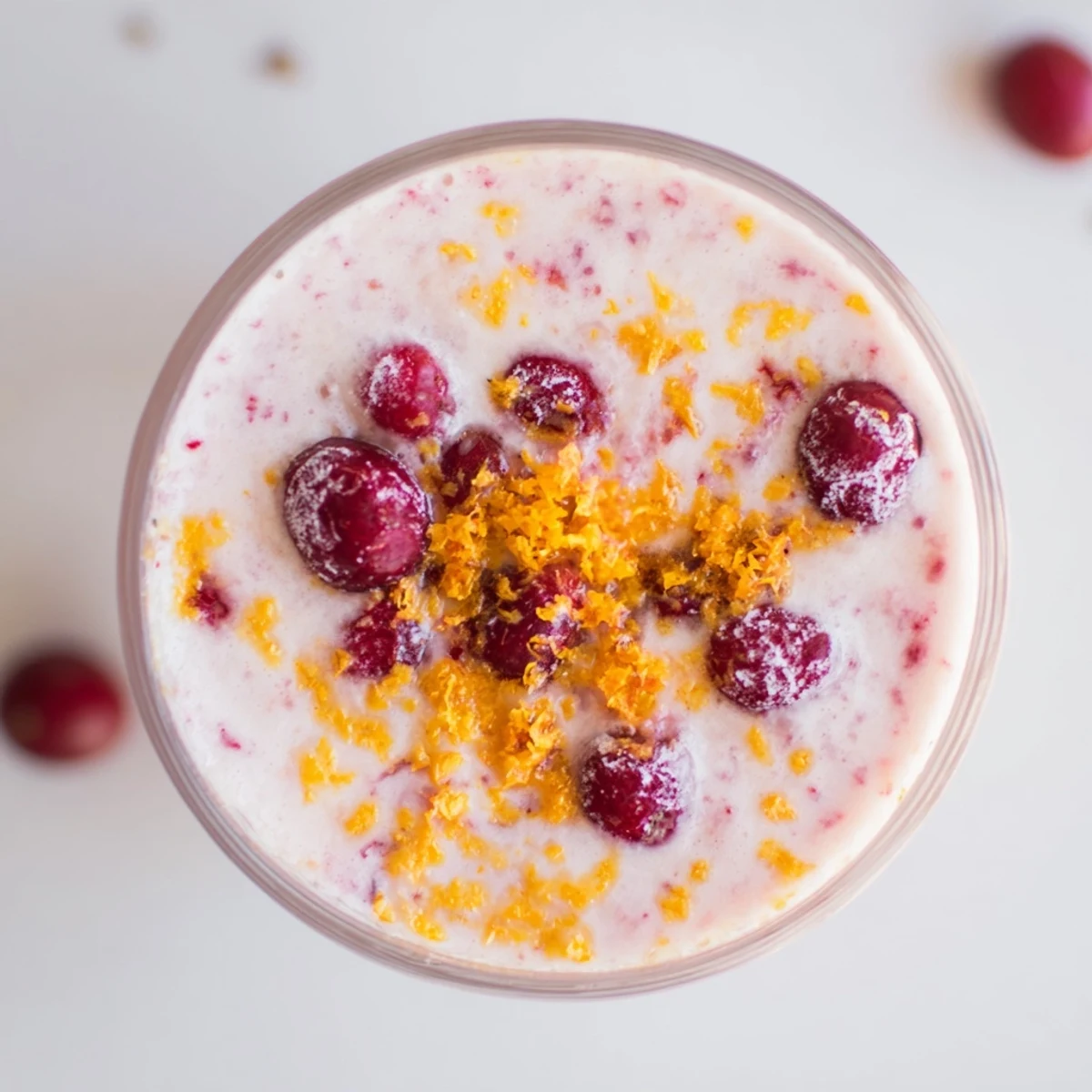 Bright orange and red smoothie with Greek yogurt, poured into a glass beside sliced oranges and fresh cranberries.