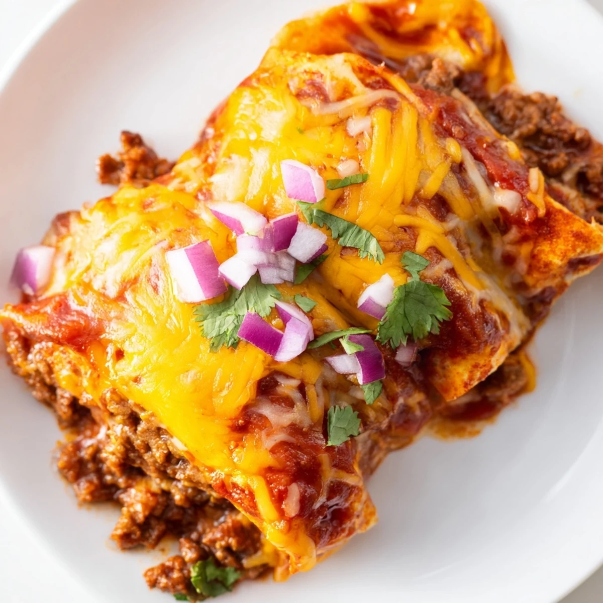 A close look at Beef Enchiladas with Homemade Red Sauce, garnished with fresh cilantro and red onion on a ceramic plate.
