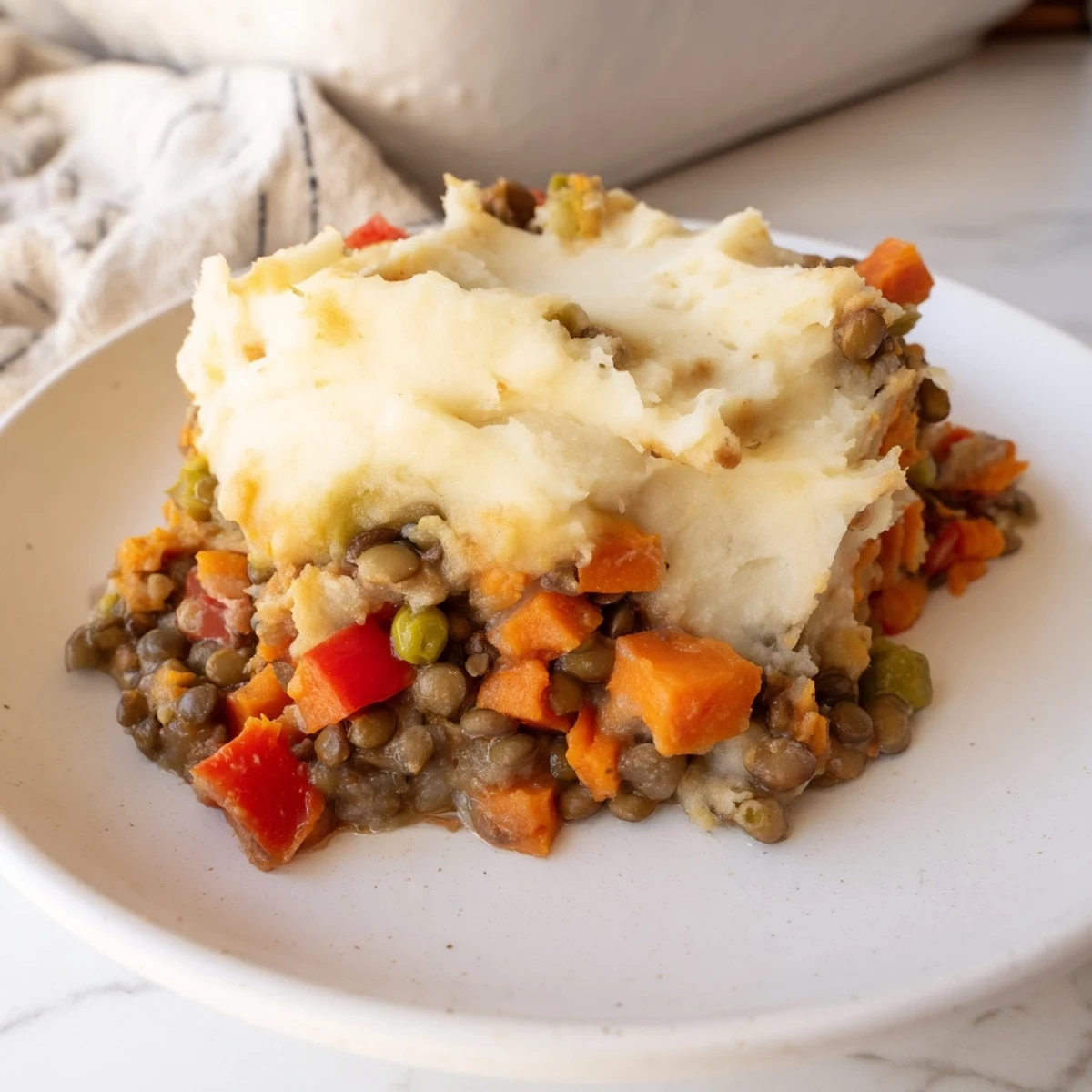 Golden Vegan Lentil and Sweet Potato Shepherds Pie with a slightly crispy orange topping, served in a white ceramic baking dish.