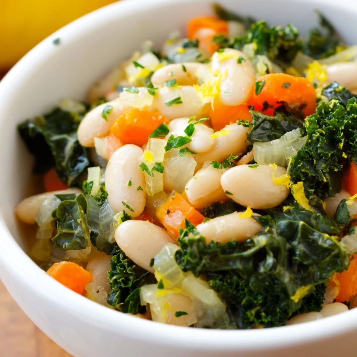 Focusing on a freshly prepared bowl of White Bean and Kale Soup with Lemon Zest, the image displays a rich vegetable broth base with tender beans and vibrant green kale leaves. A garnish of bright yellow lemon zest adds a pop of color and hints at the citrusy aroma, making the soup look hearty and inviting.