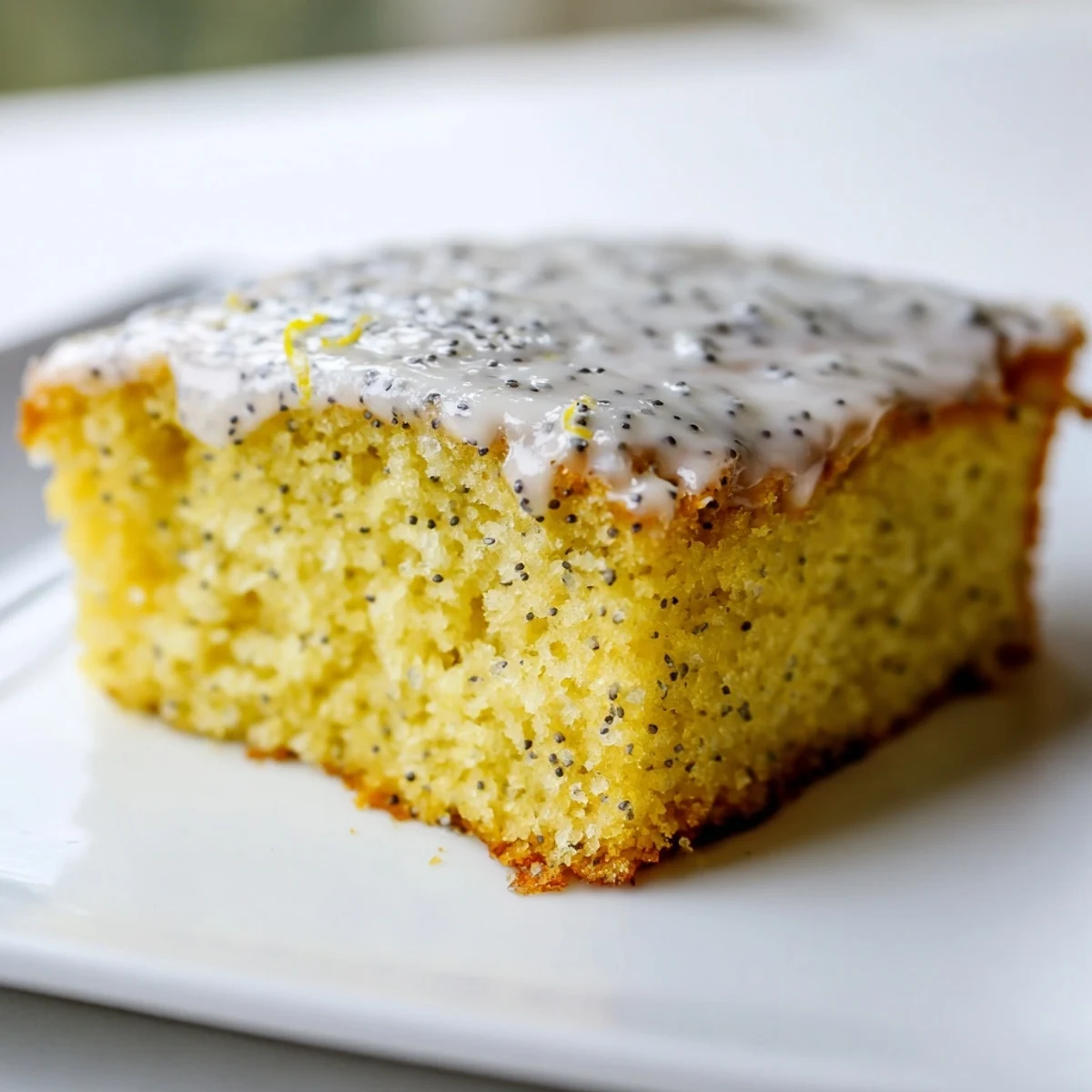A vibrant slice of Lemon Drizzle Traybake with Poppy Seeds served beside a steaming mug of Earl Grey tea.