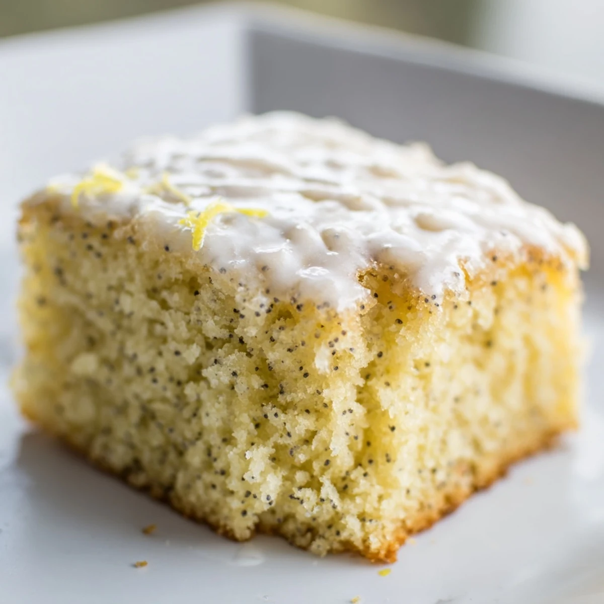 Sticky Lemon Drizzle Traybake with Poppy Seeds glistening with glaze, cut into portions on a rustic wooden board.