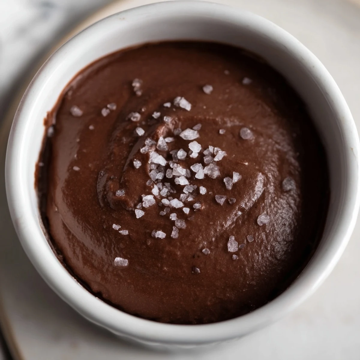Chilled dark chocolate avocado mousse in a ramekin garnished with cocoa nibs, highlighting its smooth consistency and indulgent chocolate flavor.
