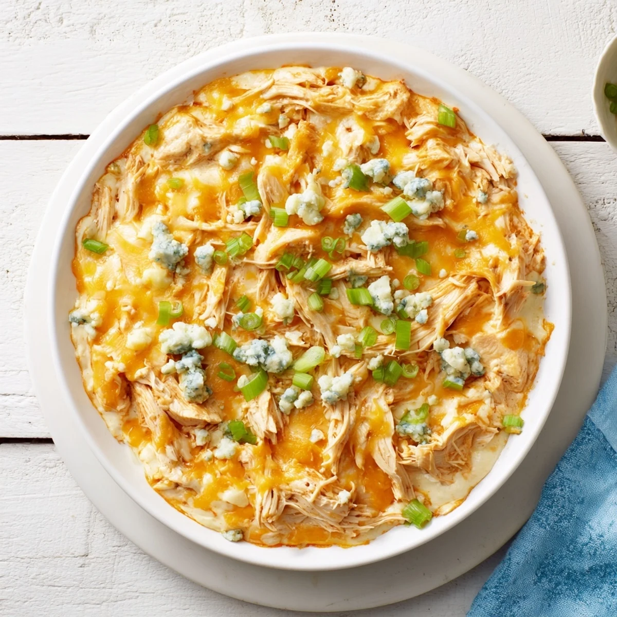 Game-day Touchdown Buffalo Chicken Dip in a baking dish, loaded with cheese and served alongside crisp carrot sticks for dipping.