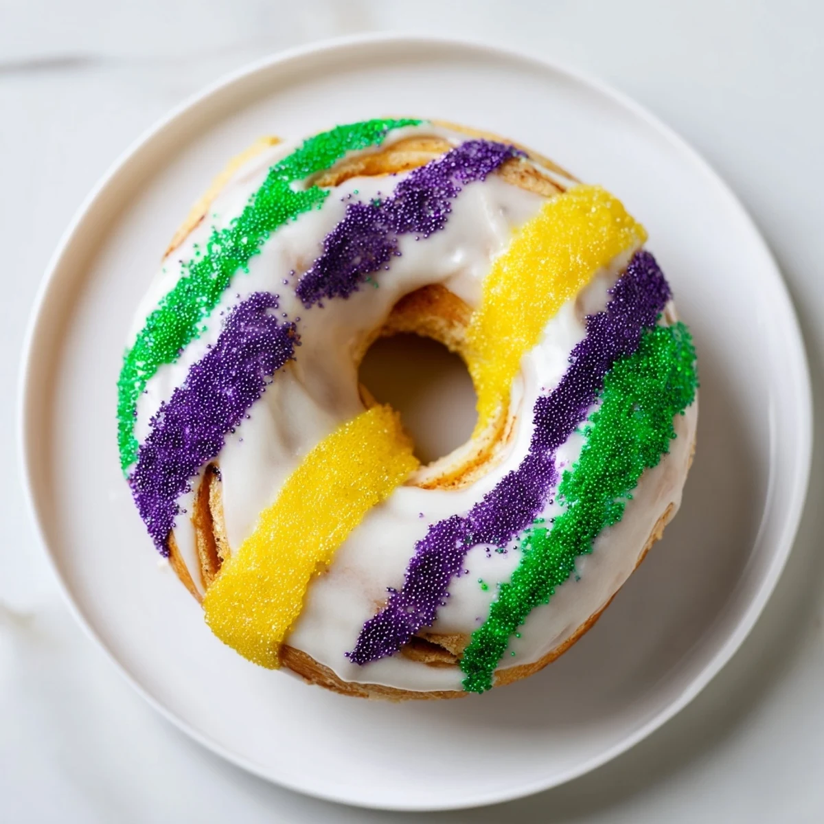 Twelve baked Mardi Gras King Cake Donuts glistening with white glaze and striped with purple, green, and yellow sugars.
