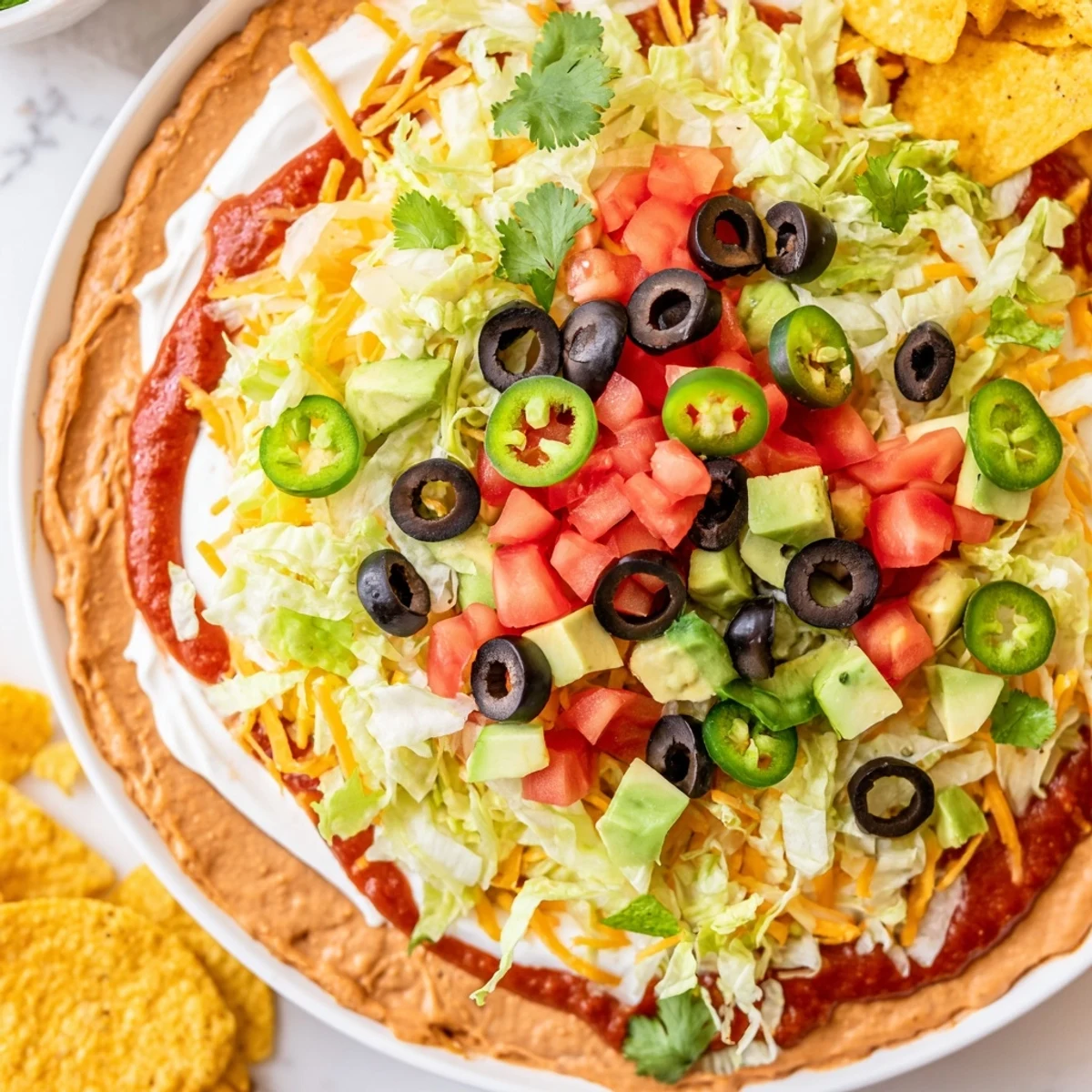 Colorful Ultimate Layered Taco Dip topped with diced tomatoes, black olives, and green onions, ready to be scooped up with crunchy tortilla chips.