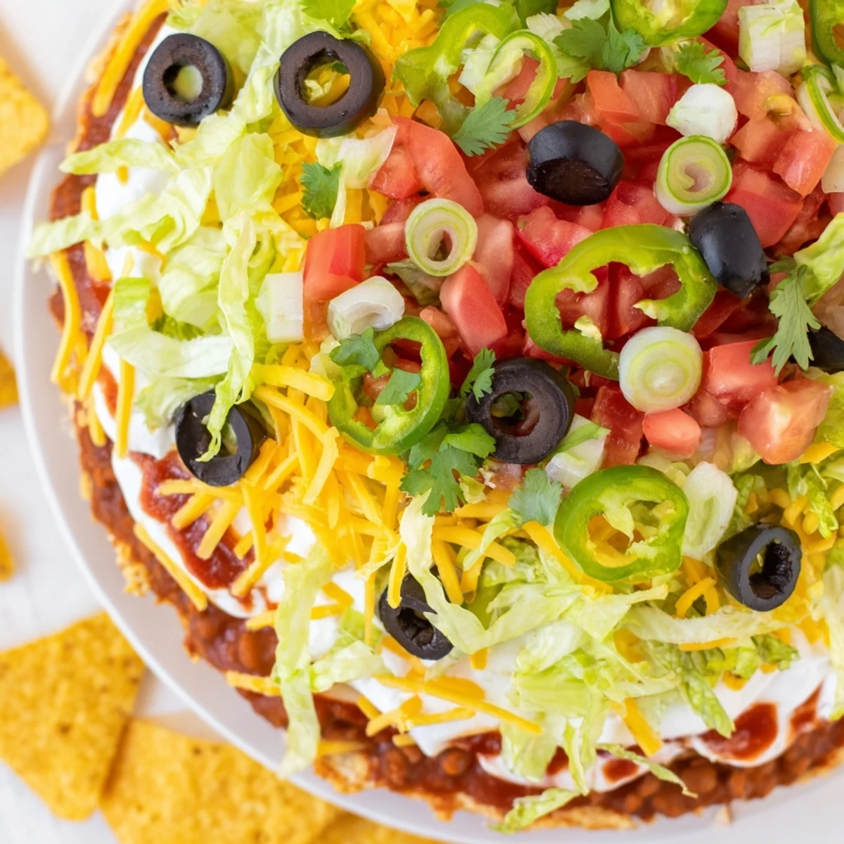 The Ultimate Layered Taco Dip is served chilled in a glass dish, featuring a thick layer of shredded lettuce and cheddar cheese.