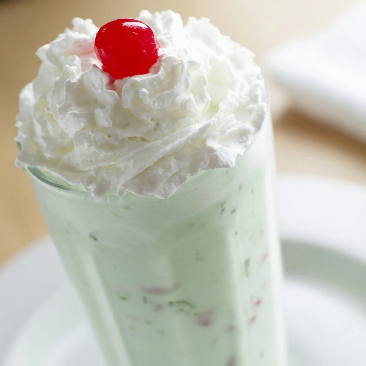 A refreshing Mint Milkshake with Maraschino Cherry served in a frosty glass, topped with whipped cream and a bright red cherry.