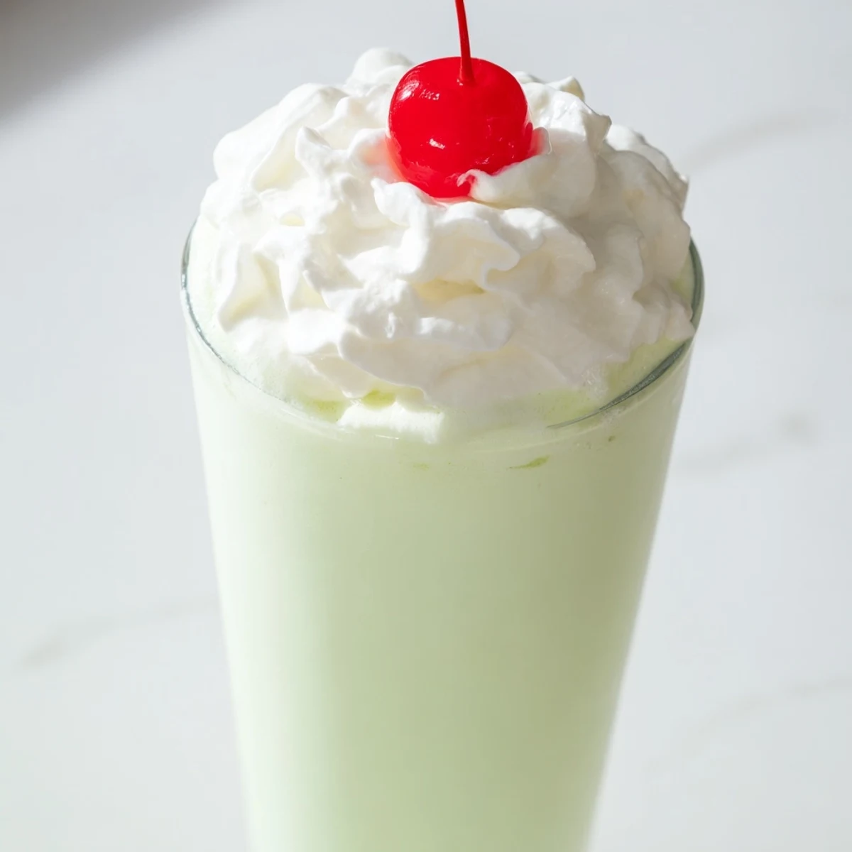 Refreshing mint milkshake garnished with a maraschino cherry, perfect for cooling down on a hot day.