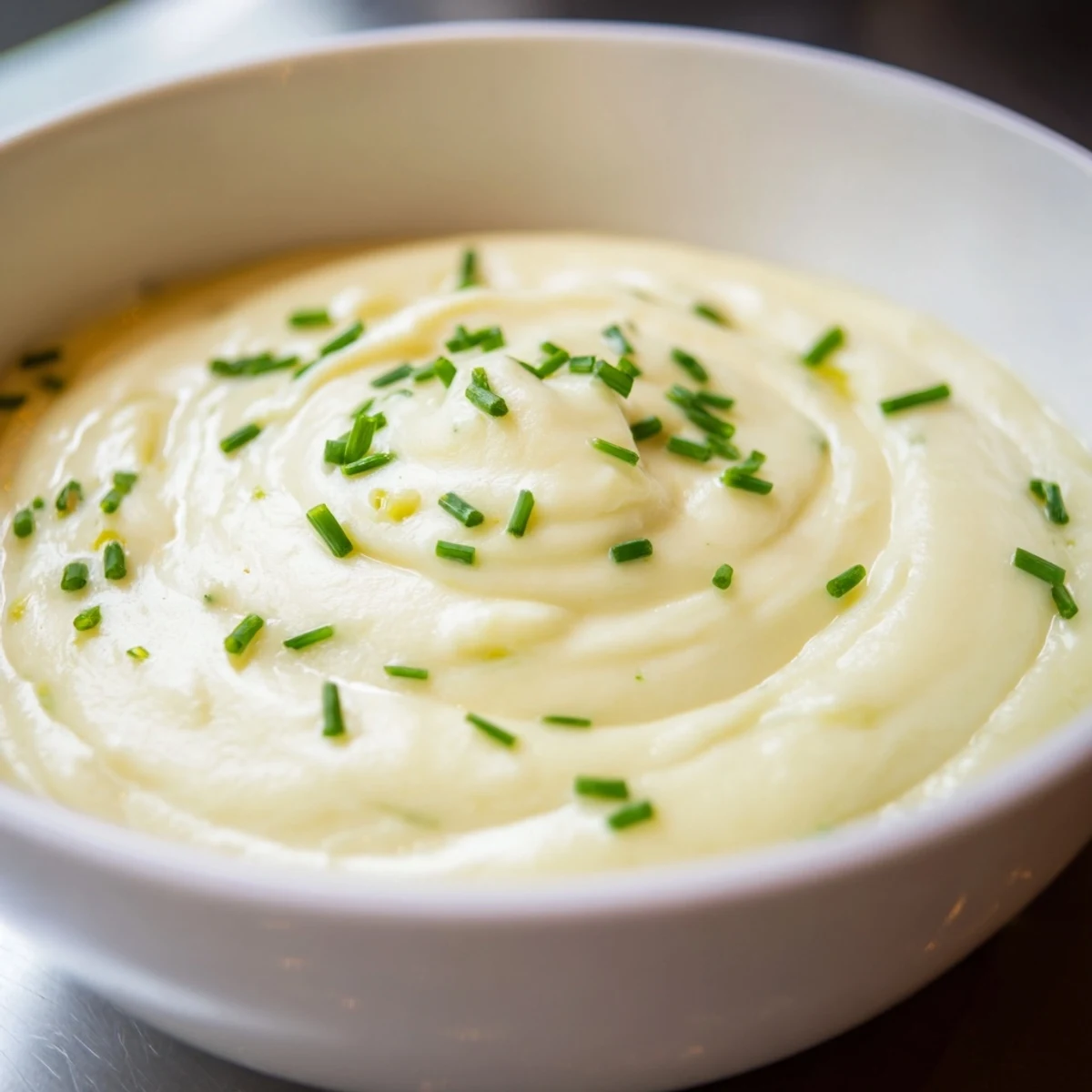Steaming creamy potato soup with chives in a white ceramic bowl, perfect for chilly evenings.