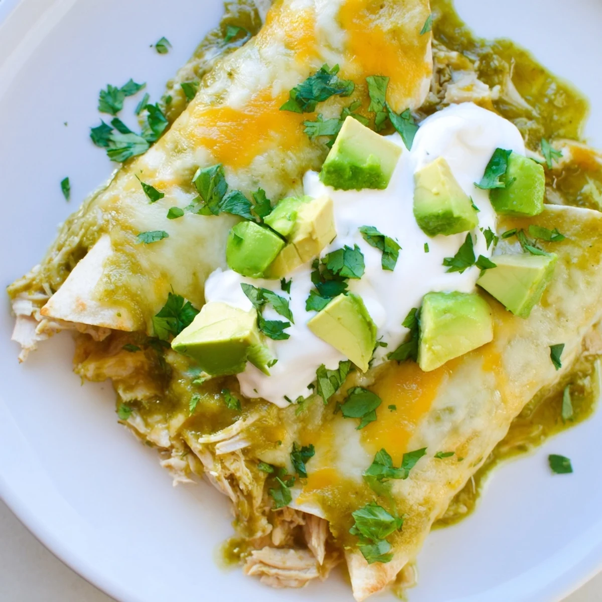 Fresh cilantro garnish on cheesy green enchiladas with chicken served with sour cream.