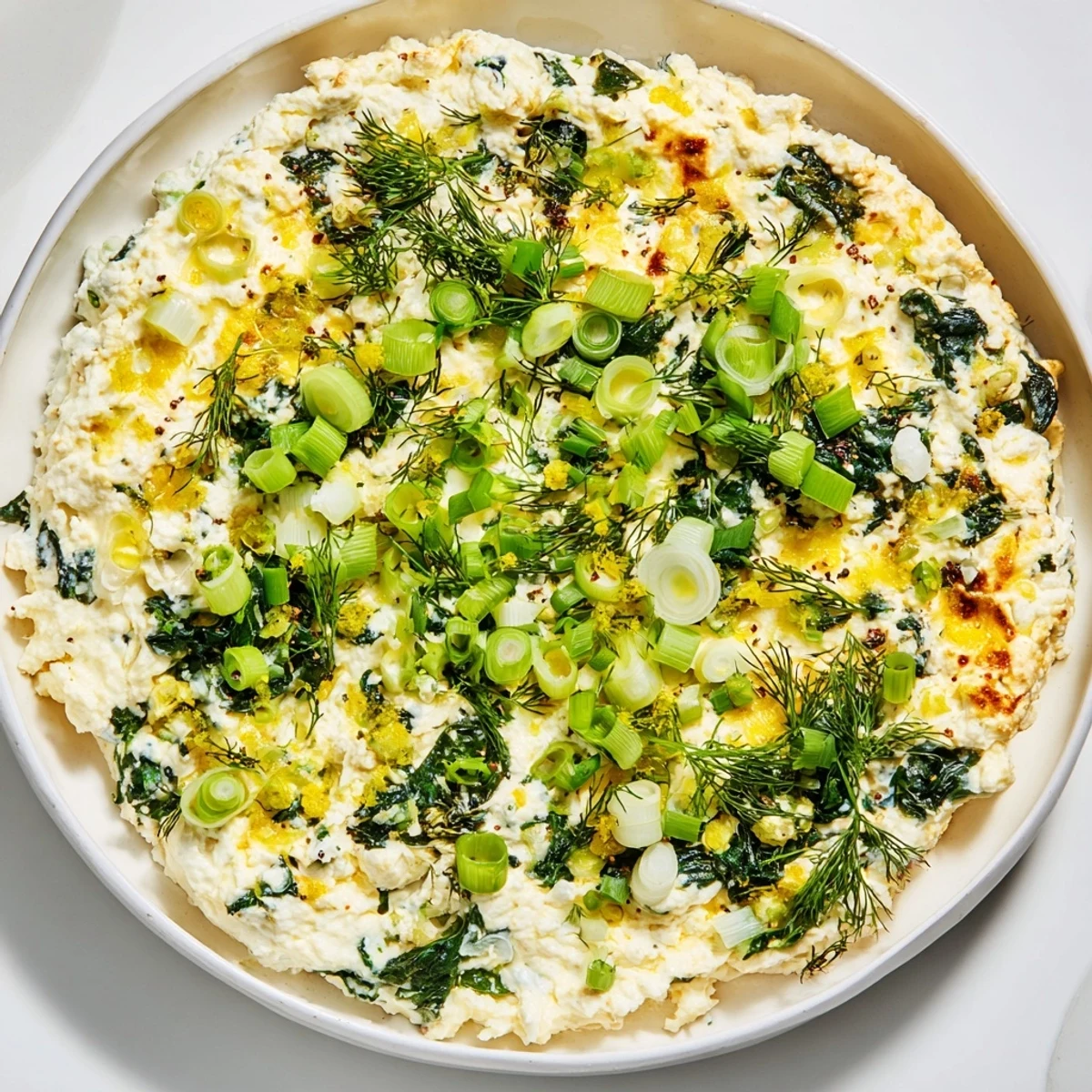 A close-up of Spinach and Pepperoncini Baked Feta Dip bubbling in a ceramic dish, with golden edges and fresh dill garnish.