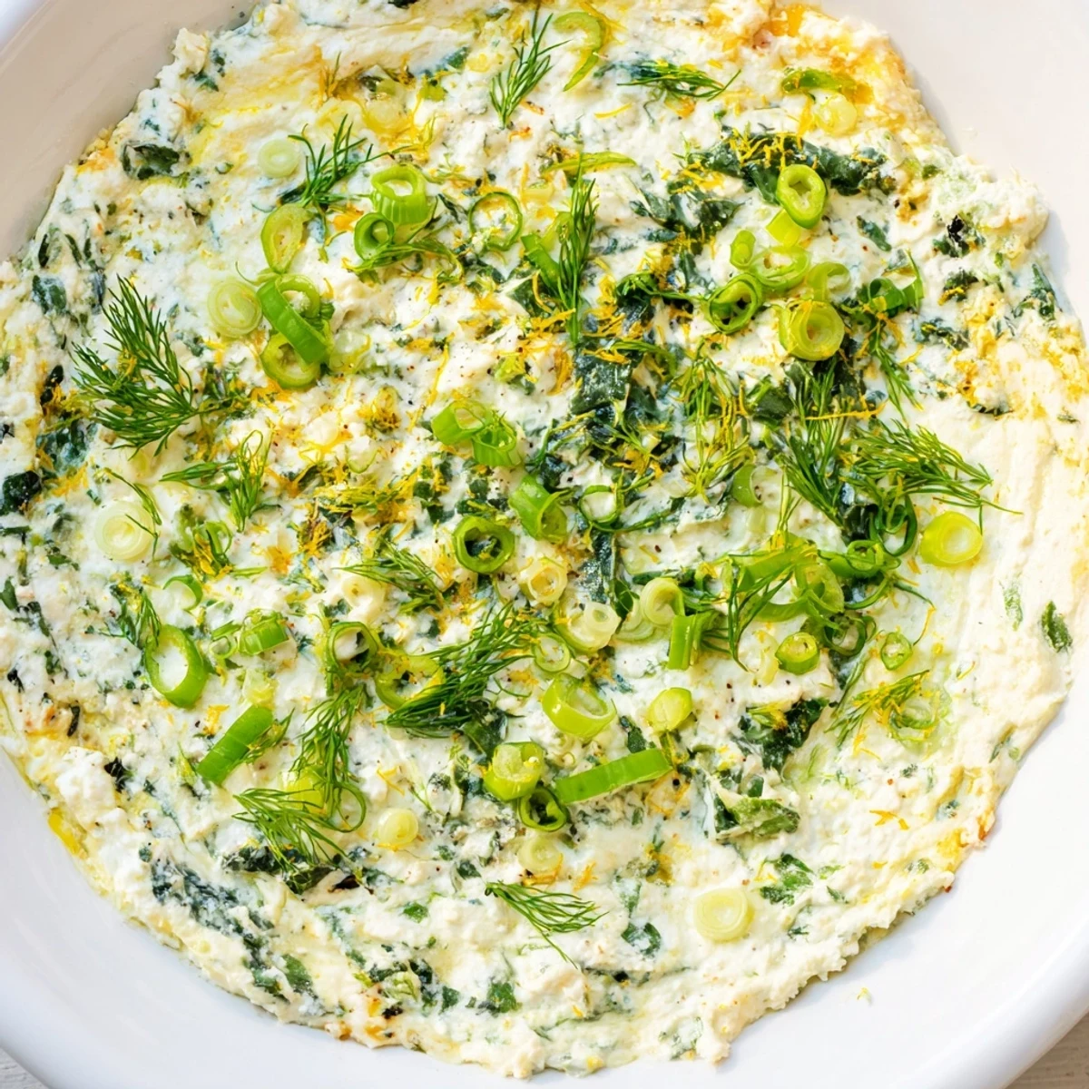 Warm Spinach and Pepperoncini Baked Feta Dip in a white dish, garnished with parsley and a lemon wedge on a marble surface.