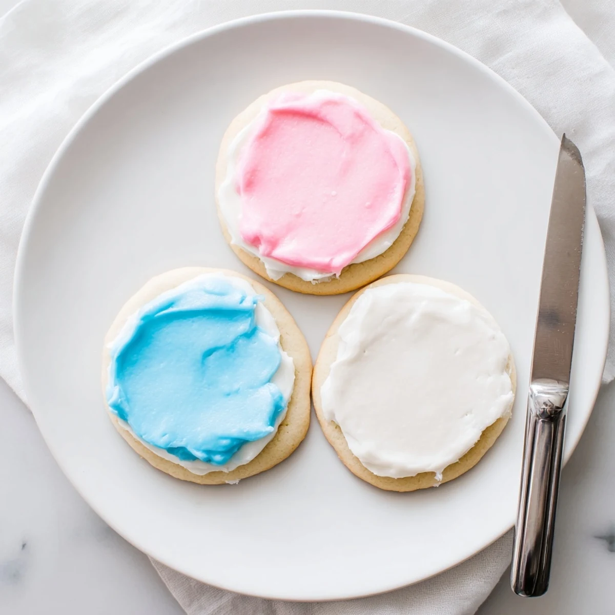A close-up of Easy Sugar Cookie Frosting with a smooth, spreadable texture and a spoon ready to ice a batch of colorful sugar cookies.