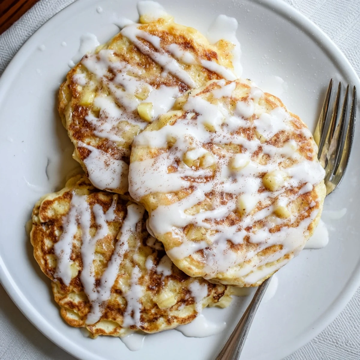 Fluffy Apple Fritter Pancakes studded with tender apples and a hint of cinnamon, drizzled with sweet glaze on a plate.