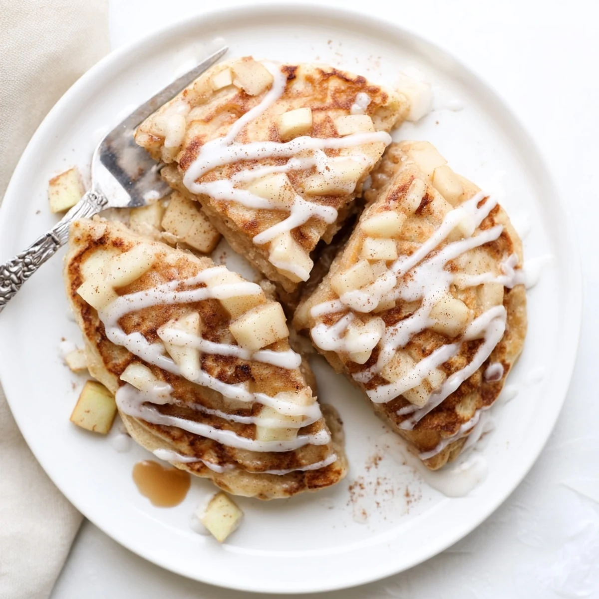 Warm stack of Apple Fritter Pancakes glistening with vanilla glaze, served alongside fresh apple slices for a cozy breakfast.