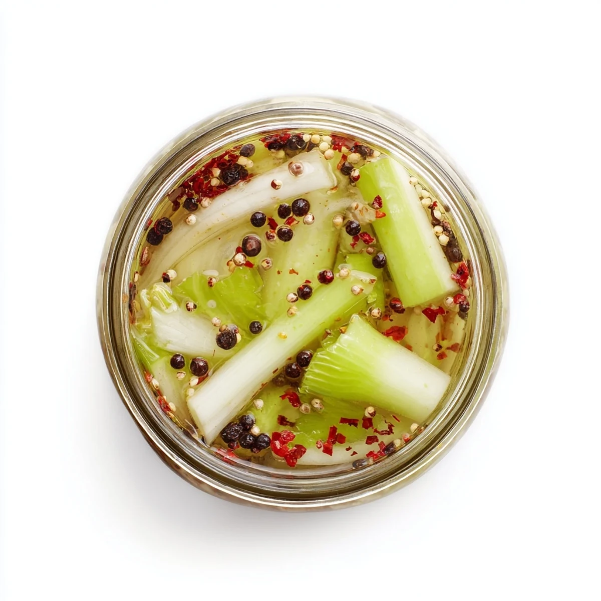 Cold Quick Pickled Celery rests in a clear jar with peppercorns and mustard seeds, perfect for snacking.