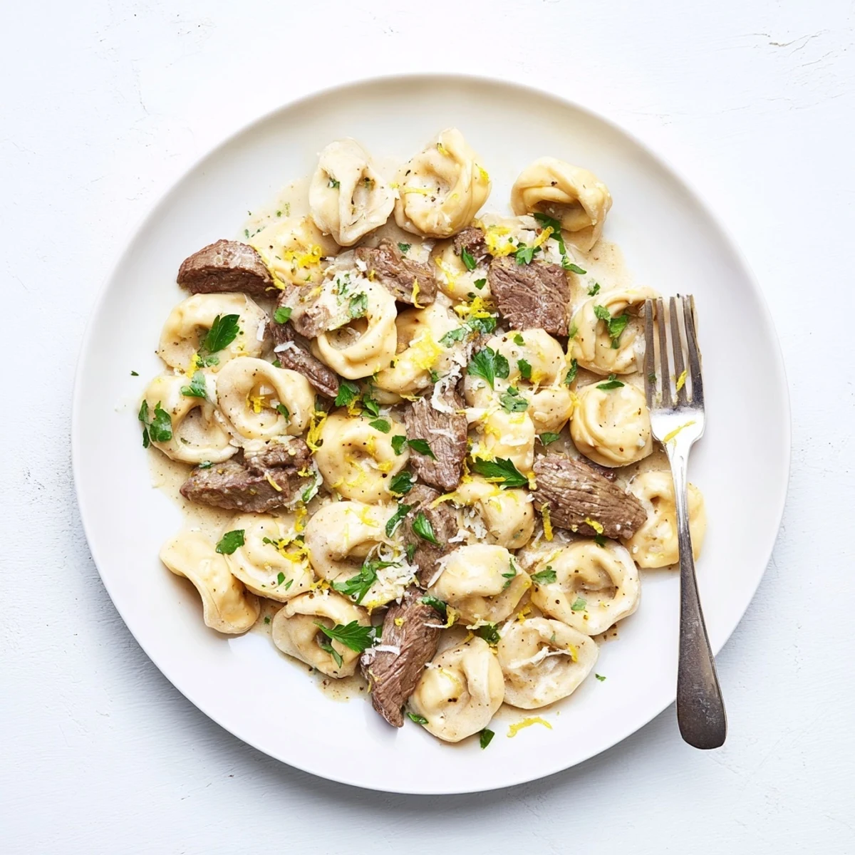 Creamy garlic-herb tortellini topped with tender sliced steak and lemon zest in a rich white sauce bowl