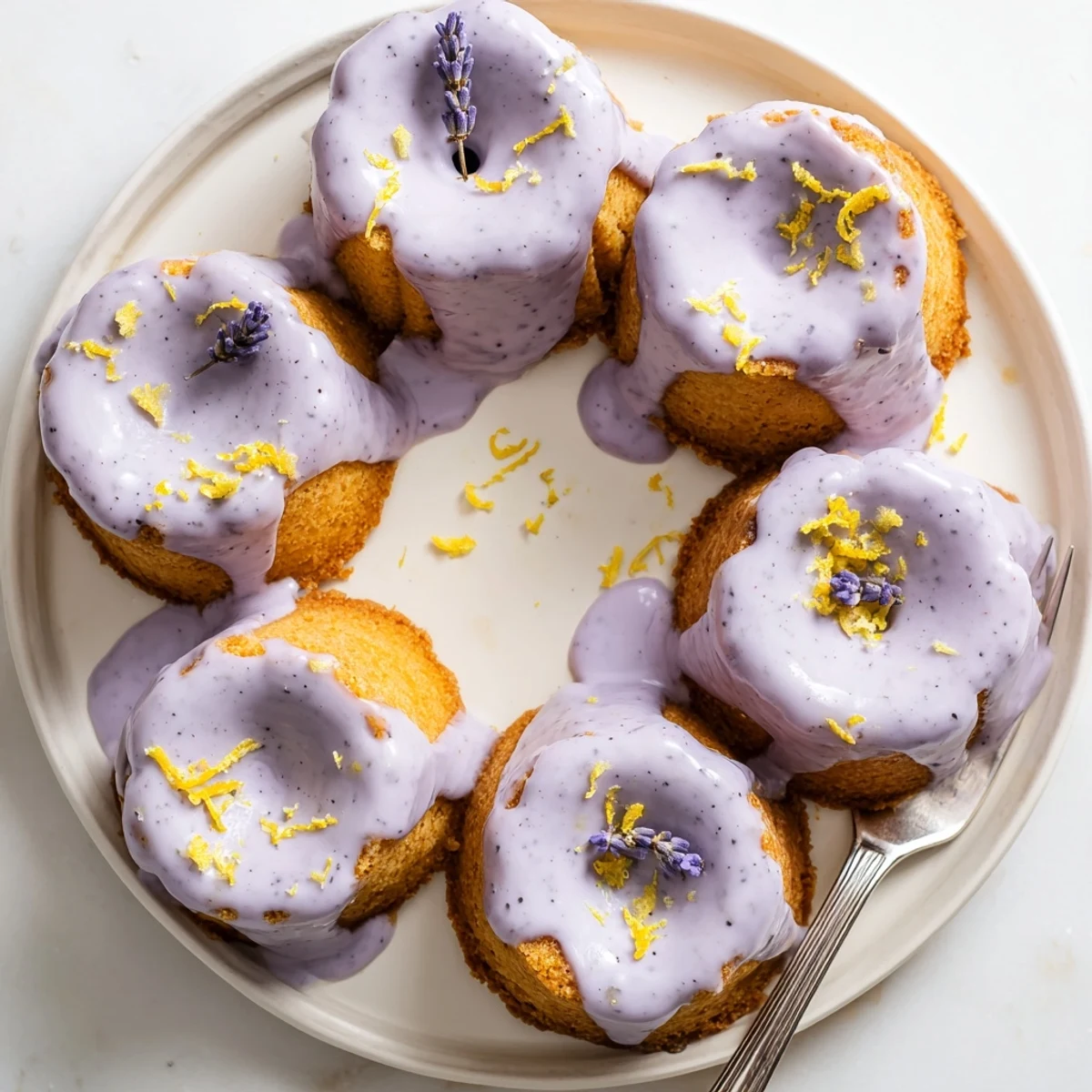 Golden mini lemon cakes drizzled with fragrant purple lavender glaze on a white plate
