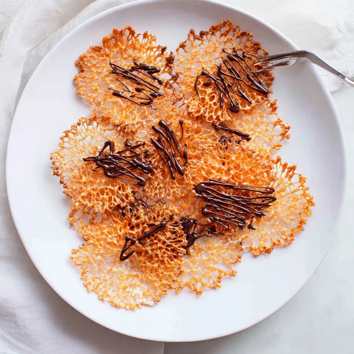 Golden brown crispy orange lace cookies spread thin with delicate lacy edges on a parchment-lined baking sheet