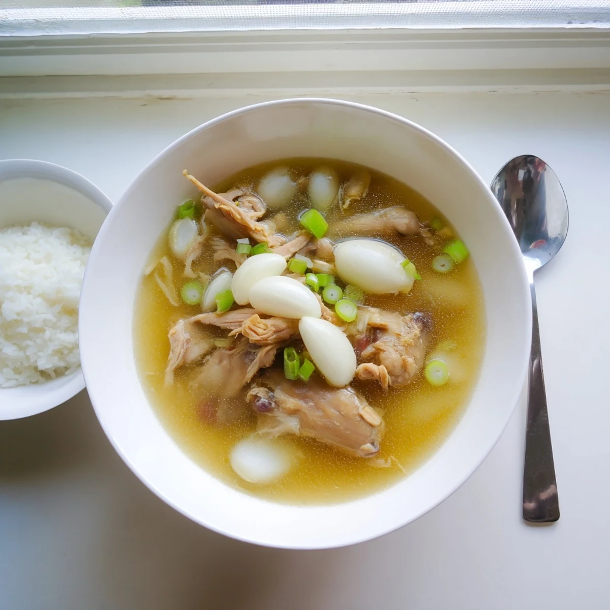 Steaming bowl of Dakgomtang Korean chicken soup garnished with fresh green onions and served alongside dipping sauce