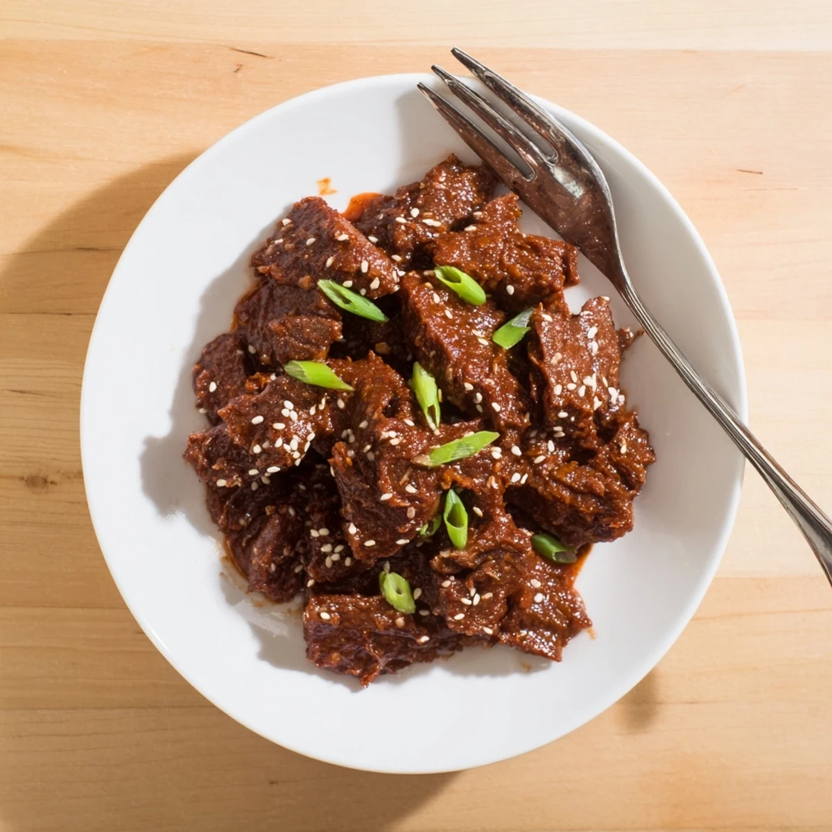 Tender slow cooker Korean beef with shredded meat coated in glossy dark sauce and garnished with green onions and sesame seeds.