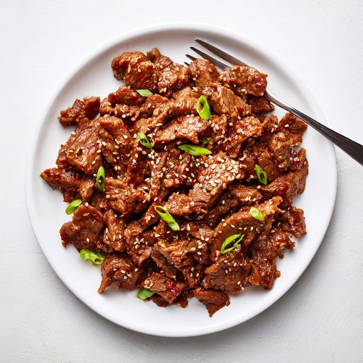 Savory slow cooker Korean beef served over fluffy white rice with extra sauce drizzled on top and crispy green onion sprinkles.