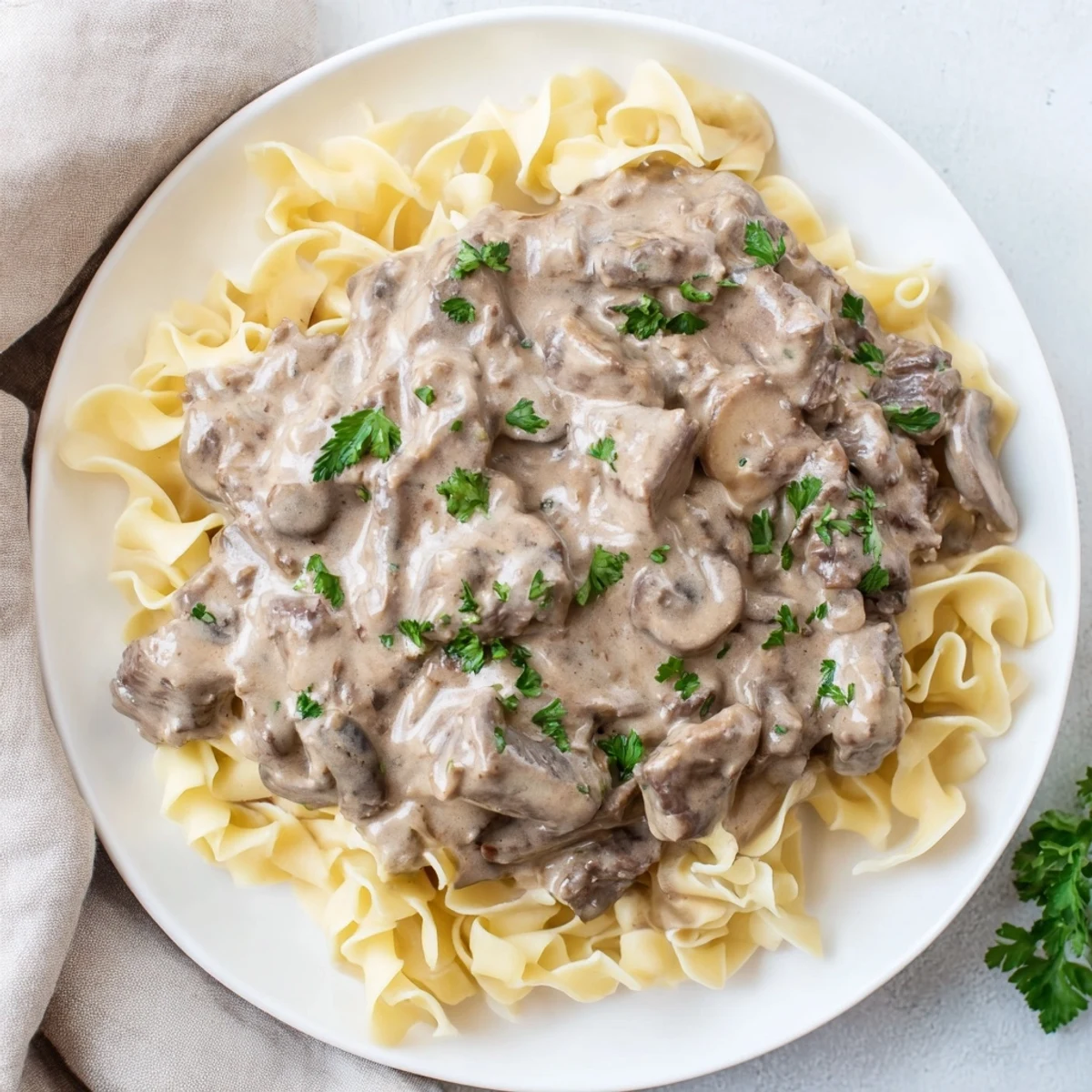 Homemade beef stroganoff in a golden creamy mushroom sauce alongside steaming egg noodles
