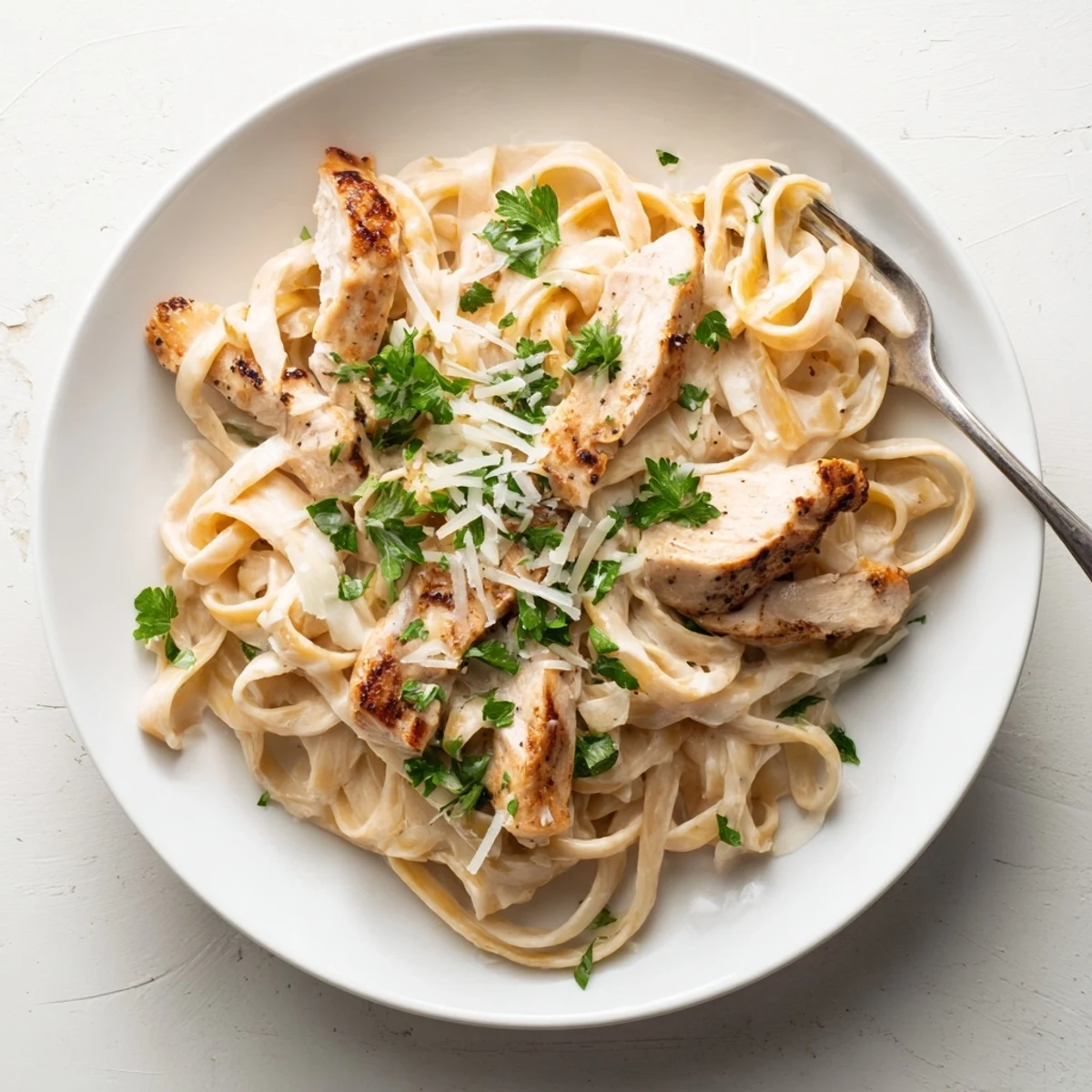 Golden sliced chicken rests atop fettuccine noodles tossed in homemade alfredo sauce with fresh parsley garnish