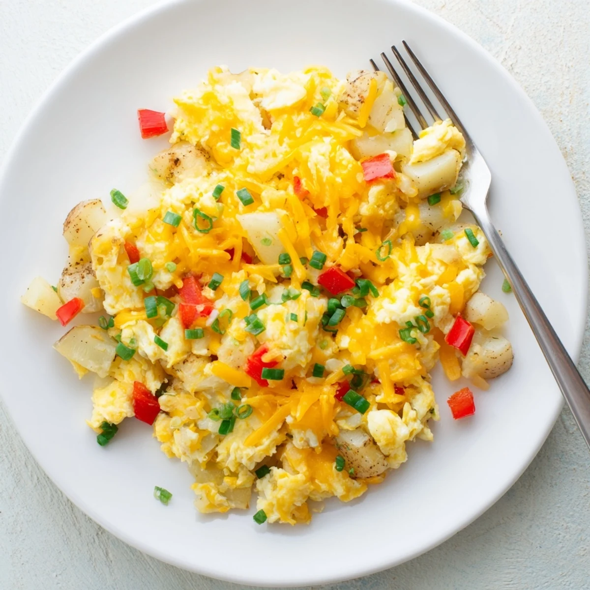 Plate of savory cheesy potato egg scramble garnished with fresh chives for breakfast