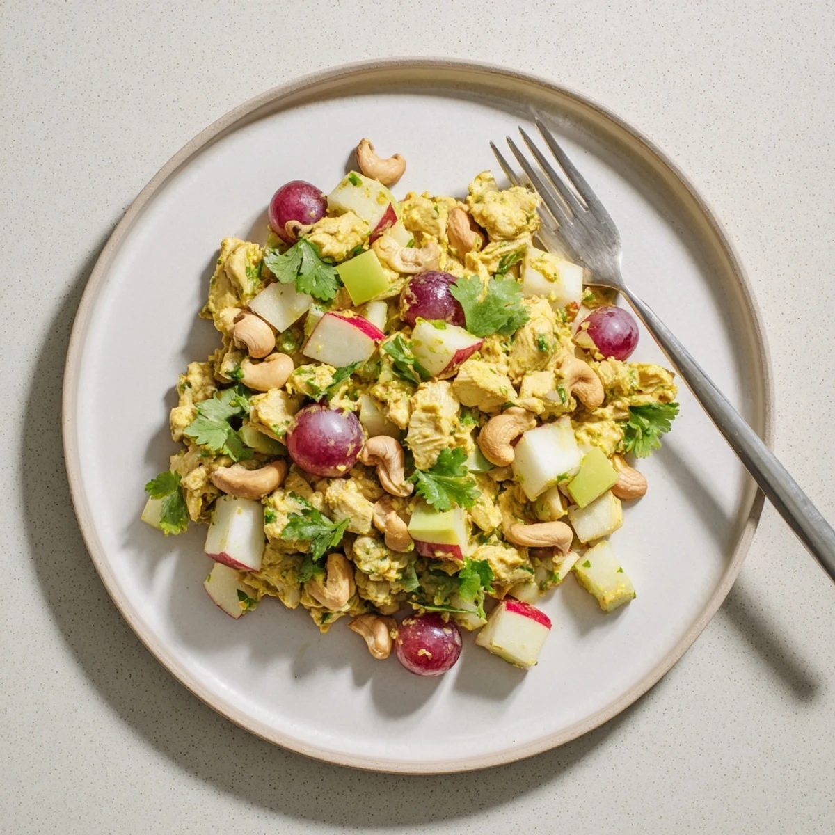 Ultimate curry chicken salad served over fresh greens with red grapes, toasted nuts, and aromatic spiced yogurt dressing