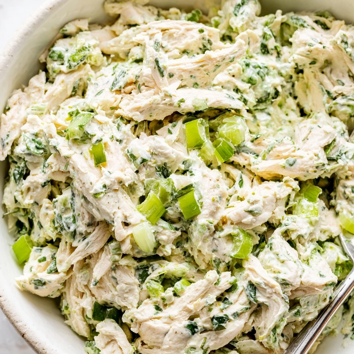 Spoonful of herbaceous green goddess chicken salad dip topped with fresh chives and celery