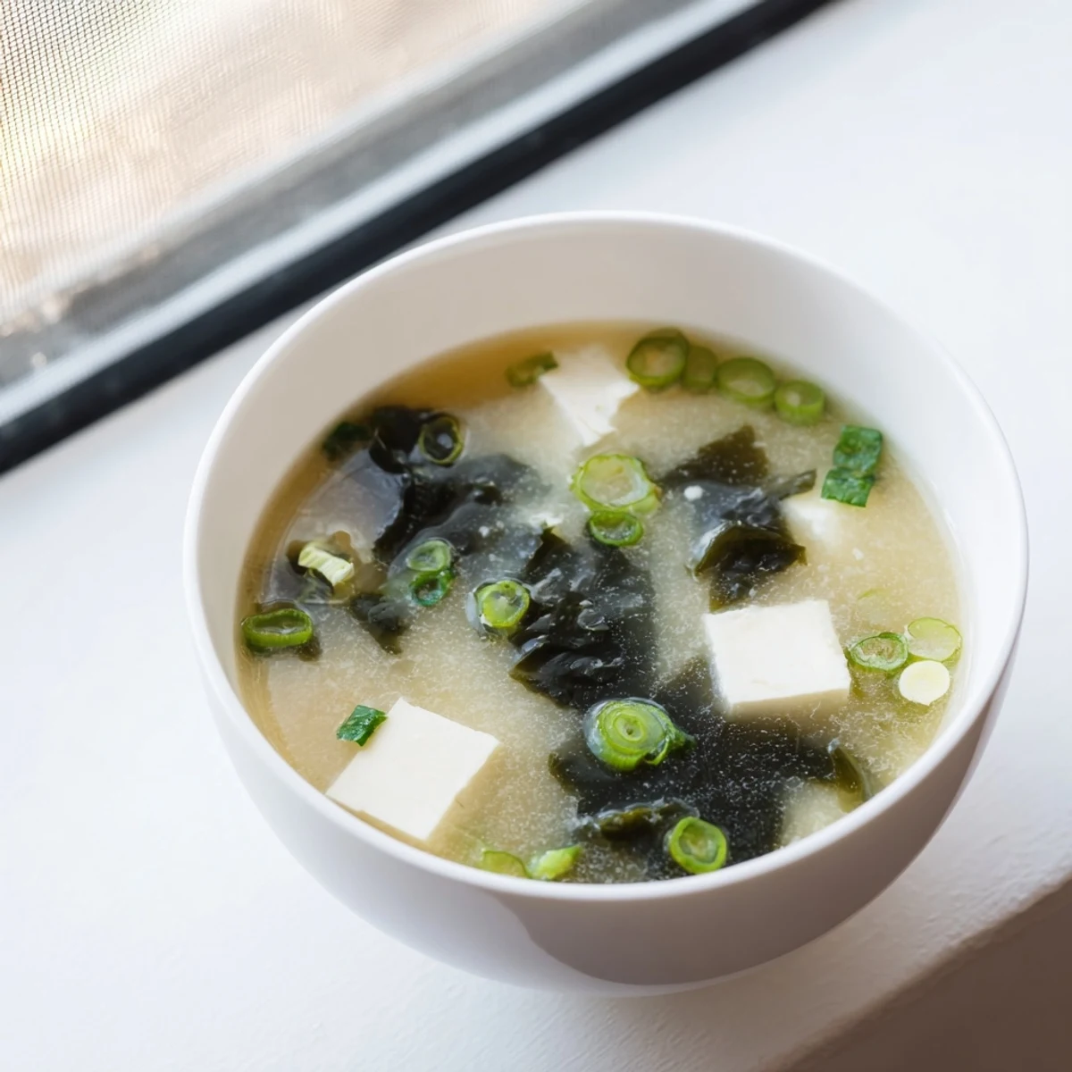 Golden easy authentic miso soup served in traditional ceramic bowl with fresh scallion sprinkles on top