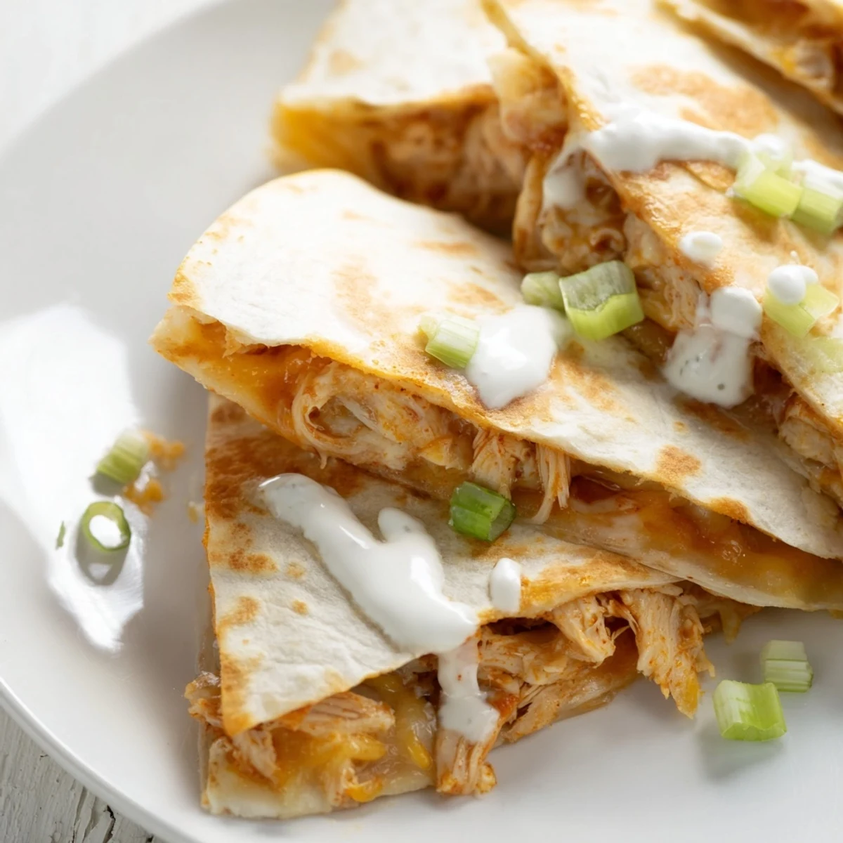 Golden brown Buffalo chicken quesadillas sliced into wedges with white ranch drizzle