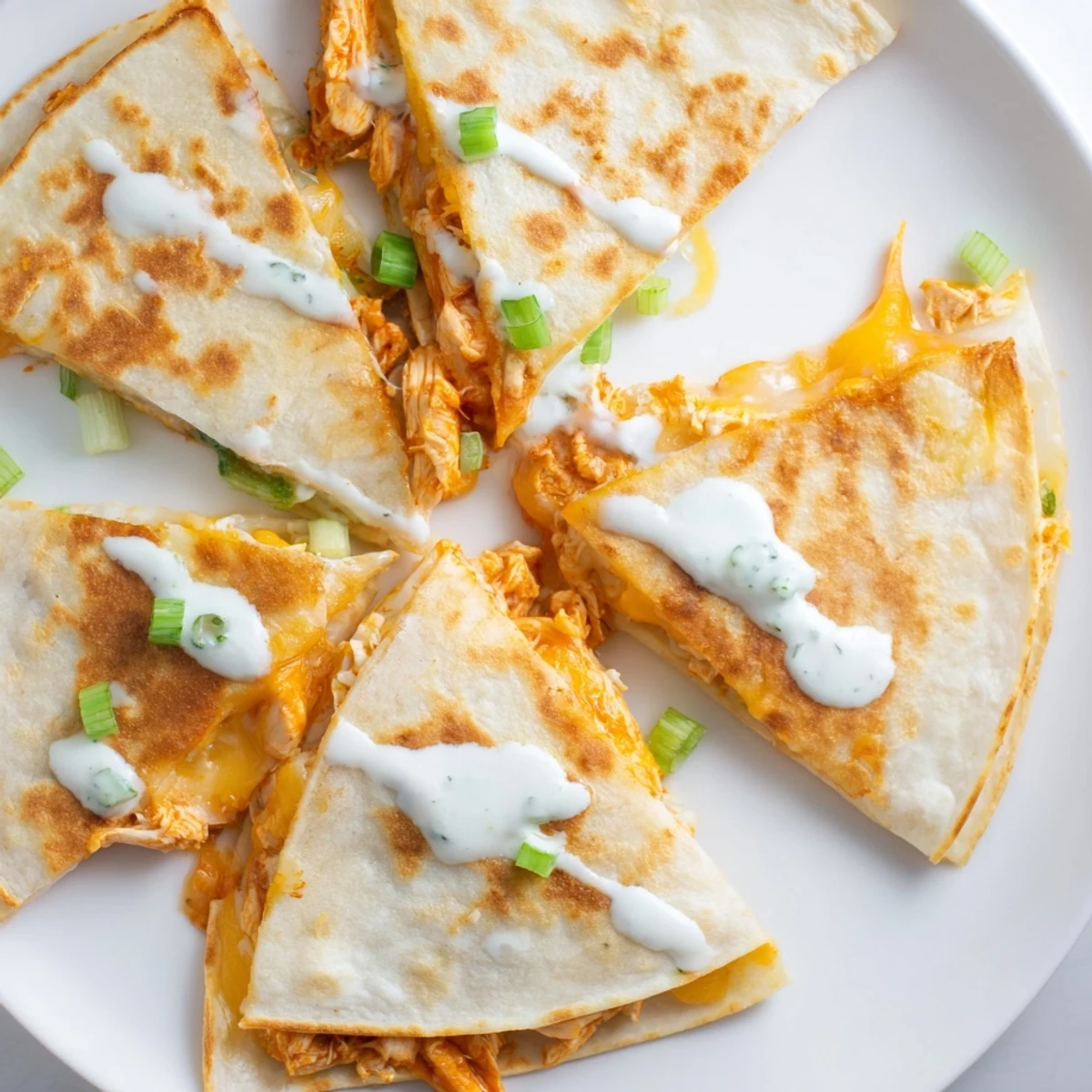 Spicy Buffalo chicken quesadillas oozing melted cheese topped with creamy ranch sauce