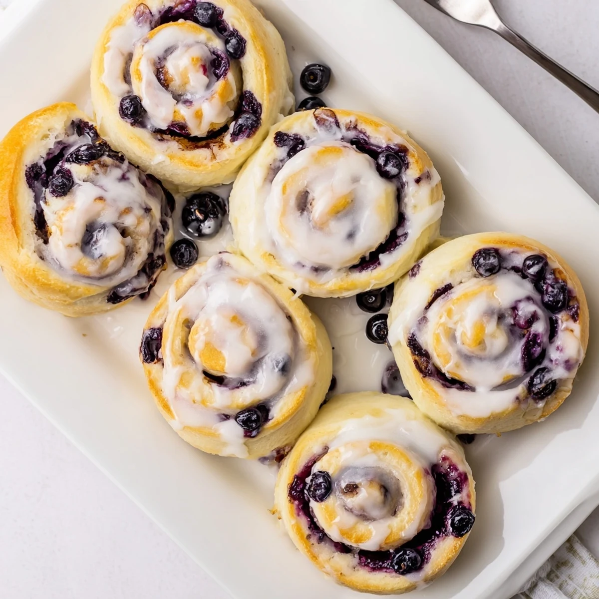 Golden lemon blueberry rolls drizzled with zesty glaze on a rustic wooden board