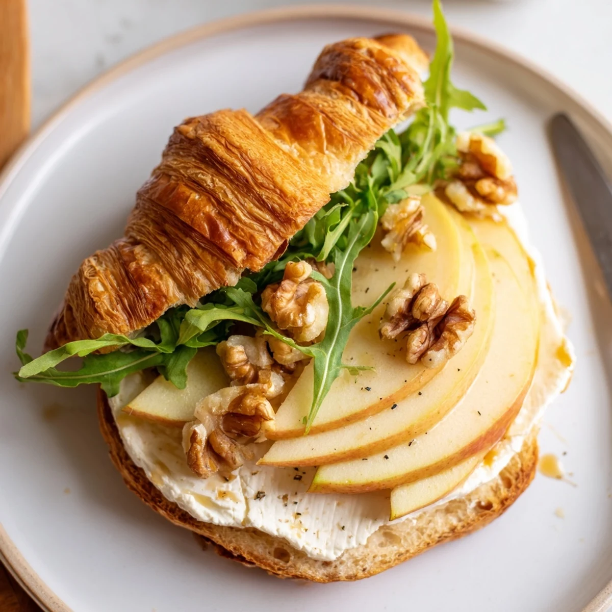 A lightly toasted Apple Goat Cheese Croissant Sandwich served with honey drizzle