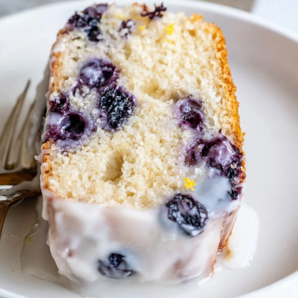 Golden slice of lemon blueberry cake on a white plate with powdered sugar dusting