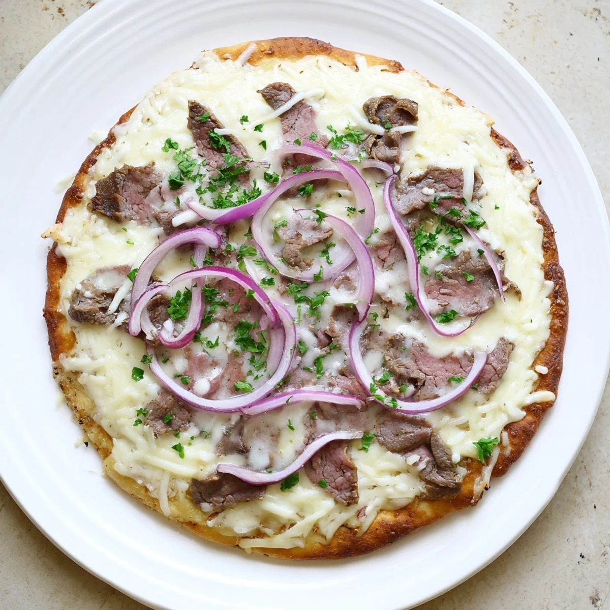 Sliced steak atop creamy Alfredo sauce on this American-Italian fusion pizza featuring mozzarella, provolone, and red onion toppings
