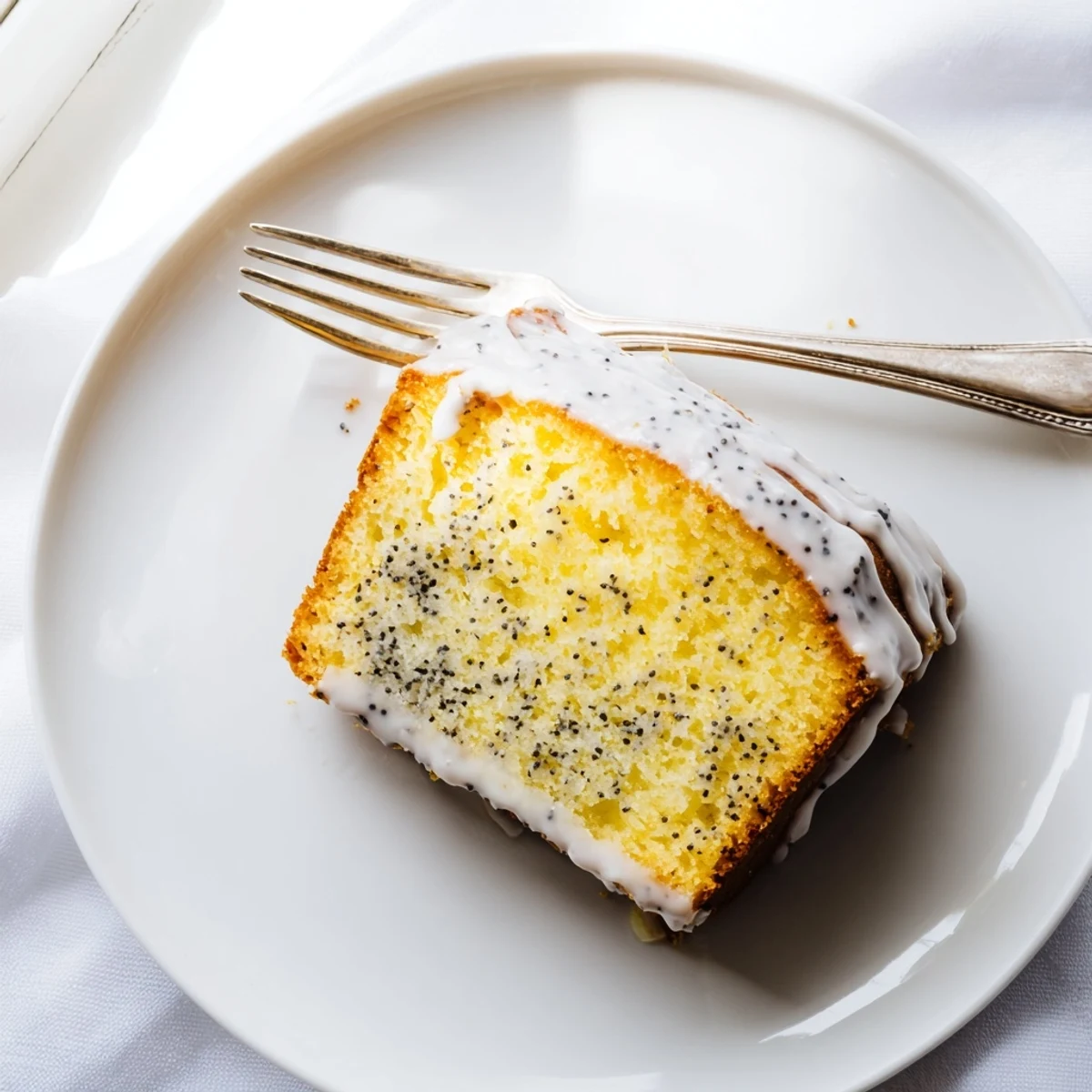 Moist lemon poppy seed cake slice speckled with crunchy seeds and topped with tangy icing