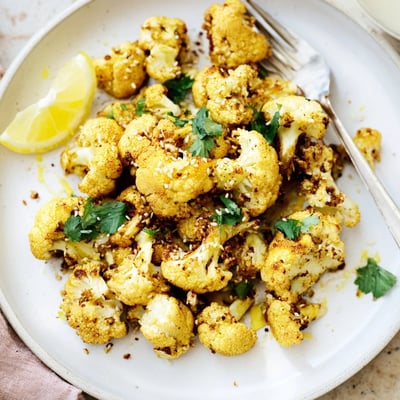 Roasted cauliflower with turmeric, served warm and garnished with cilantro and toasted sesame seeds for extra flavor.