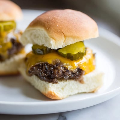 Freshly grilled Beef Sliders with Cheese and Pickles stacked high, topped with tangy pickles and served alongside crispy fries.