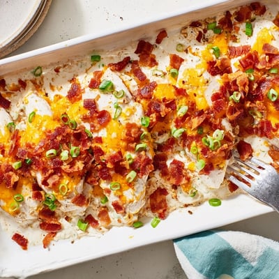 Golden baked crack chicken with bubbling cheese and green onion garnish on a white plate