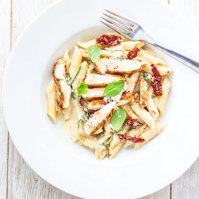 Golden seared chicken breast pieces tossed with penne pasta in rich garlic cream sauce topped with fresh basil and parmesan