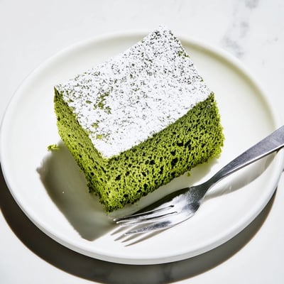 Slice of Japanese-inspired matcha cake bake served on a white plate with tea  
